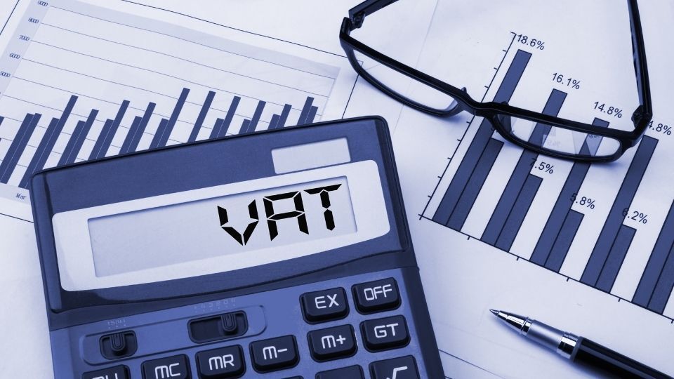 (In the image a calculator can be seen showcasing VAT and percentages in the back) What is the VAT Flat Rate Scheme and How Does it Work
