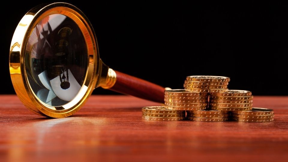 (In the image the concept of a magnifying glass and money showcases financial investigations)