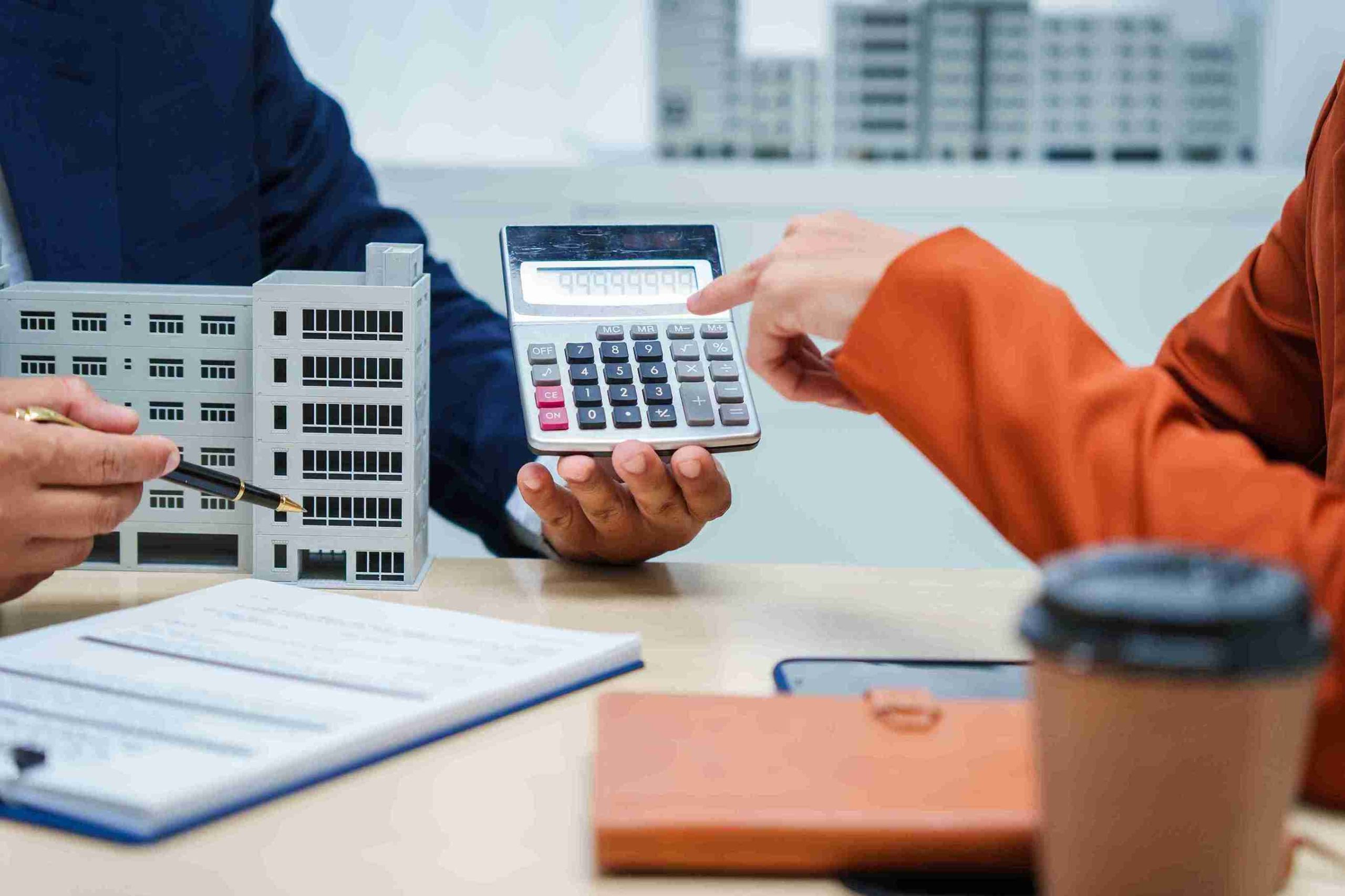 Two people examine a building model, one holding a calculator and the other a paper with design details.