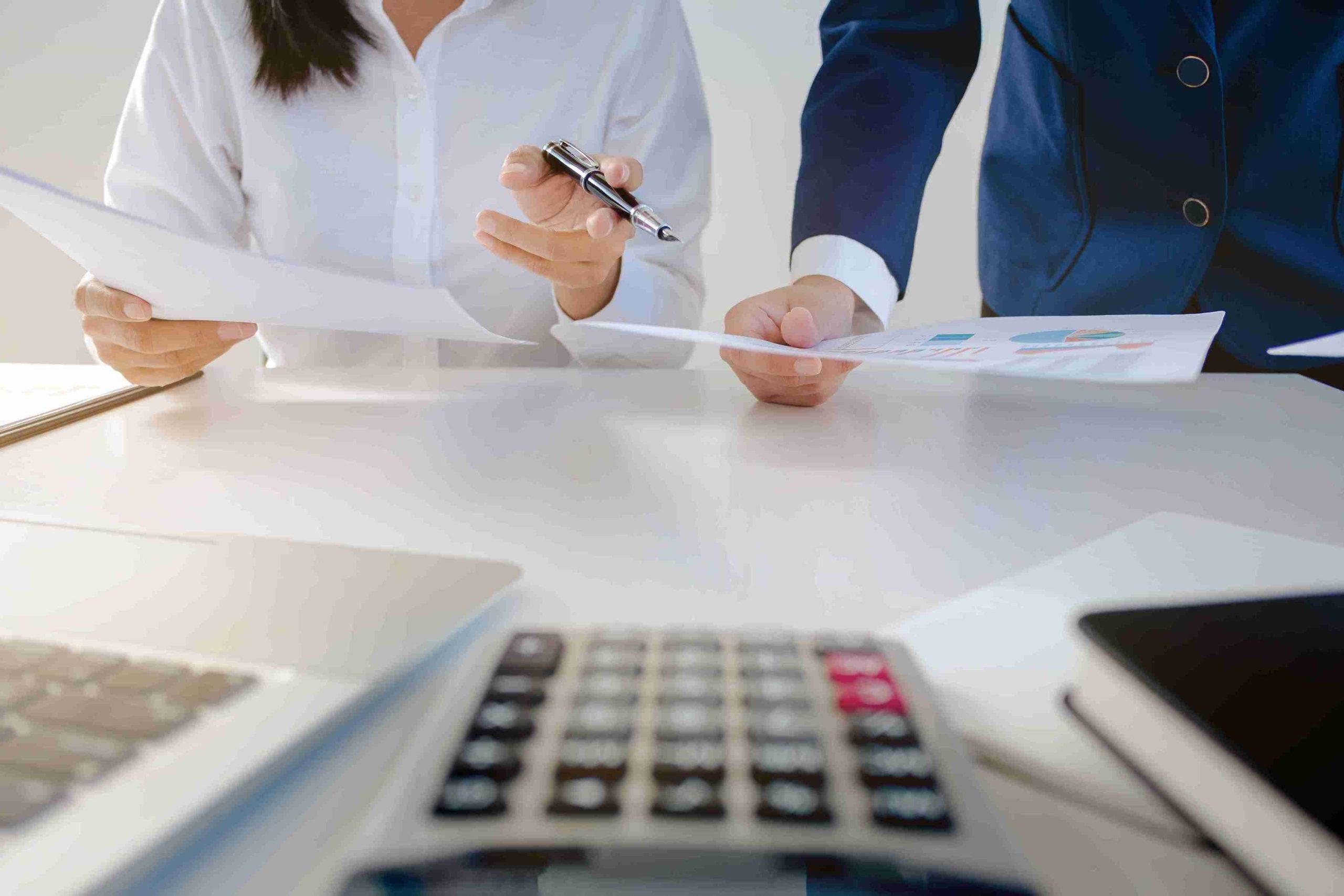 Two people collaborate on paperwork at a desk, focused on their tasks in a well-lit office environment.