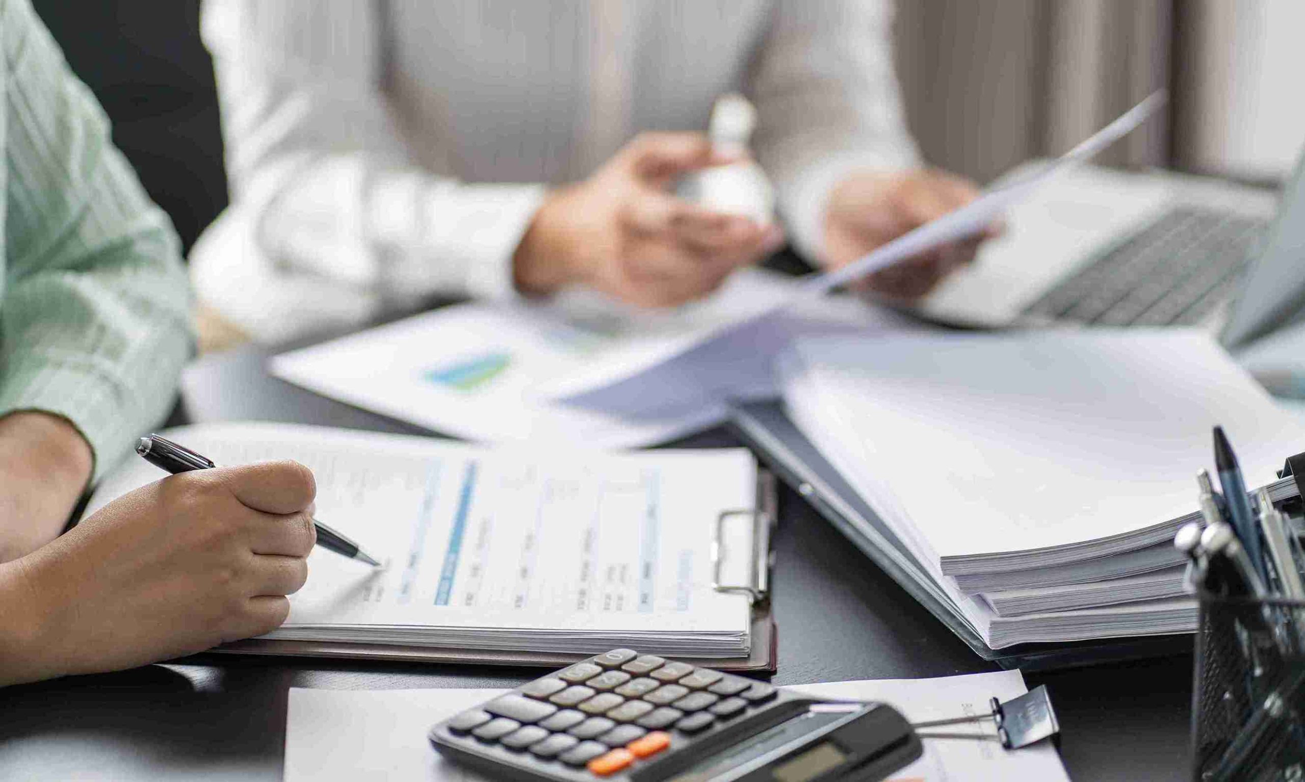 A business person reviews paperwork while using a calculator on a desk, focused on their financial tasks.