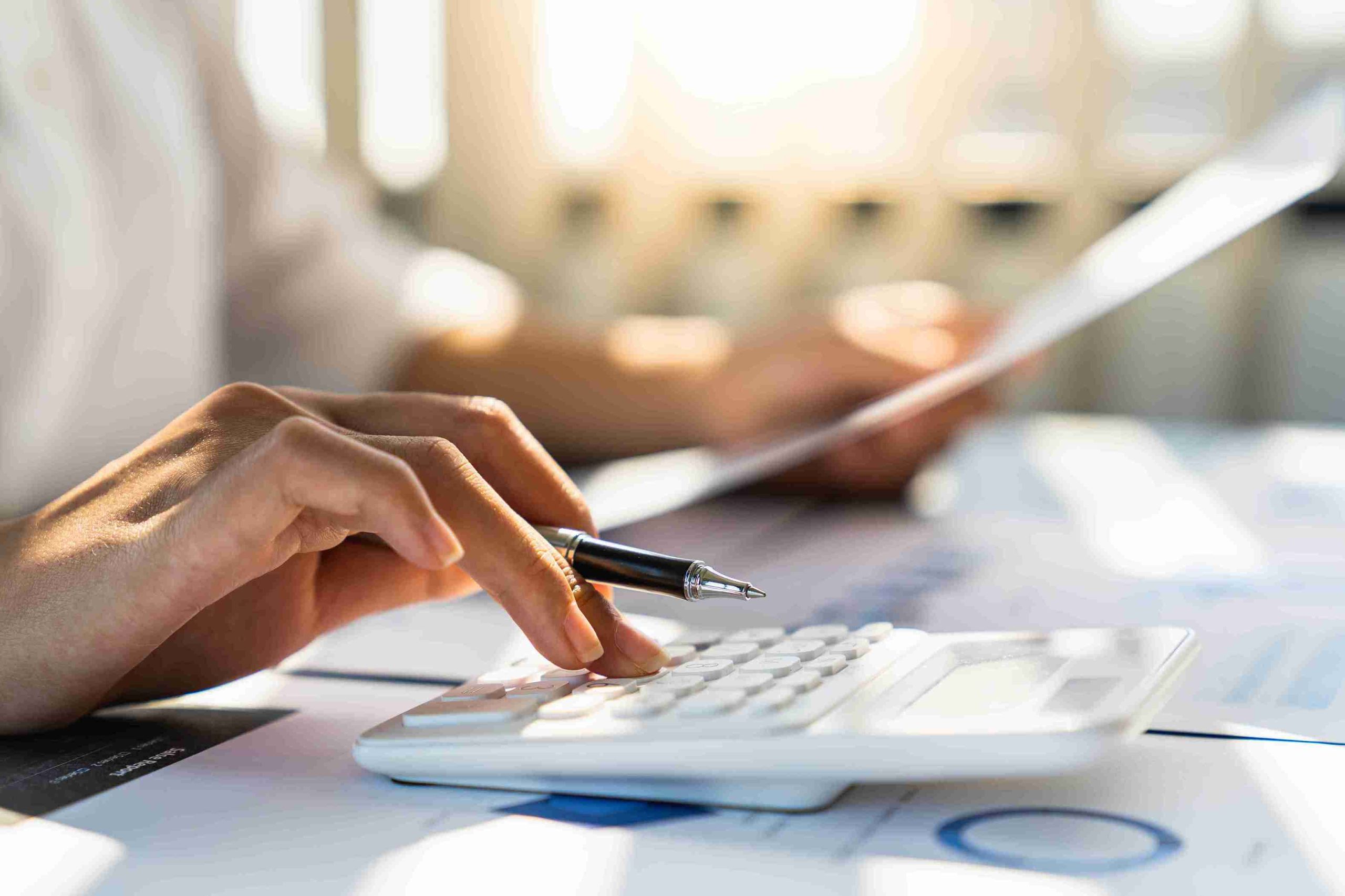 A person focused on a calculator, diligently calculating numbers on a bright desk.
