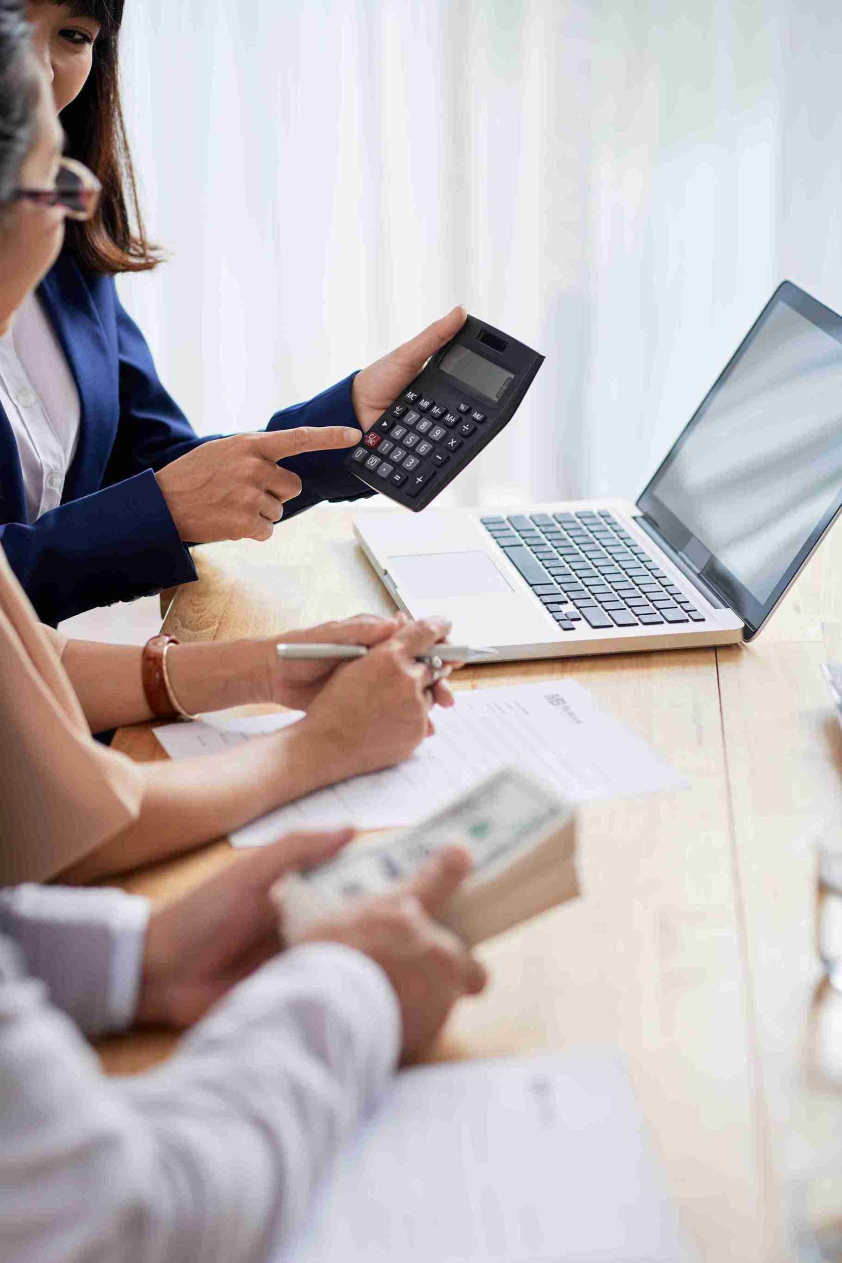 A diverse group of people collaborating at a table with a laptop and calculator, focused on their work.