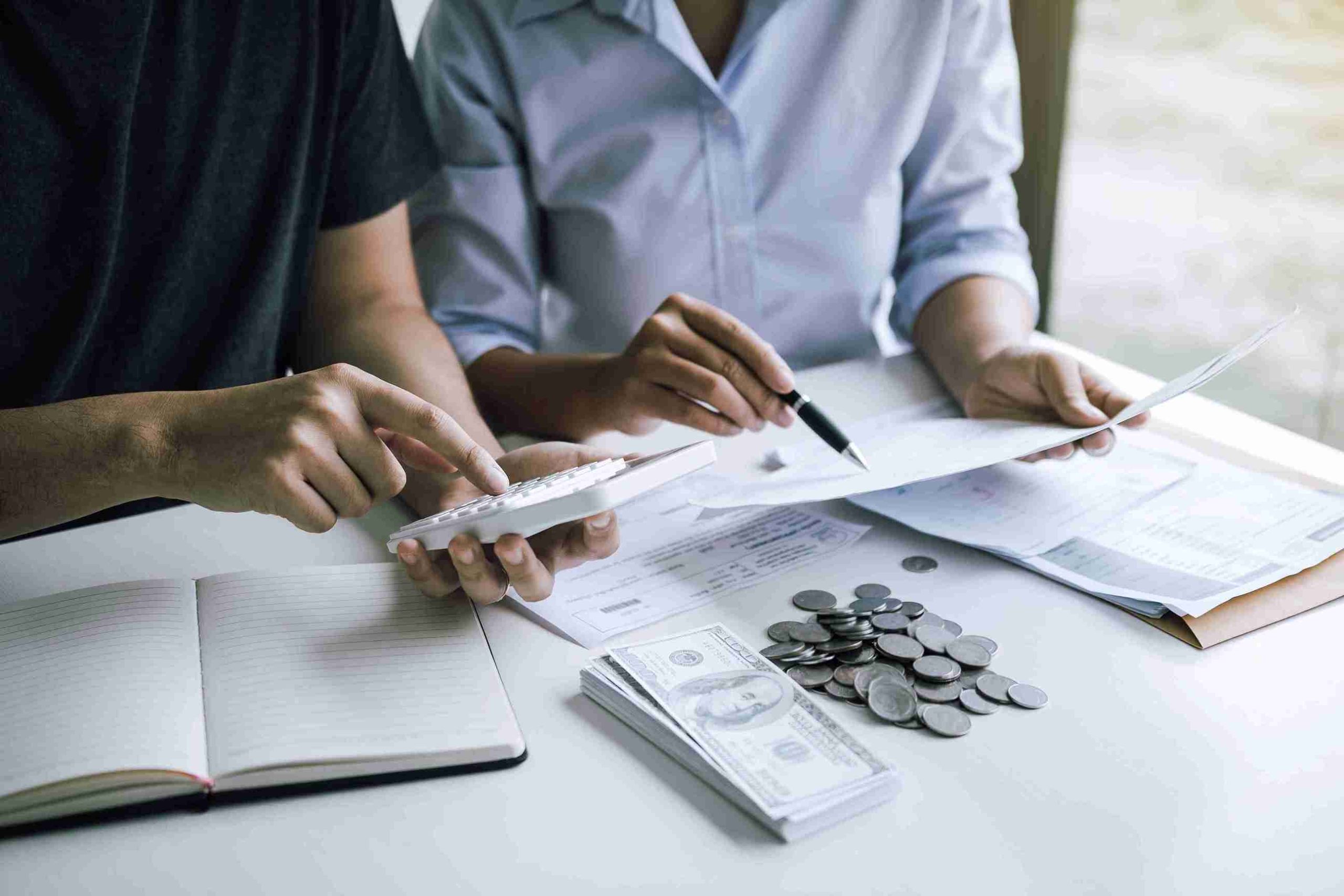 Two people sit at a table, discussing money and papers, with focused expressions on their faces.