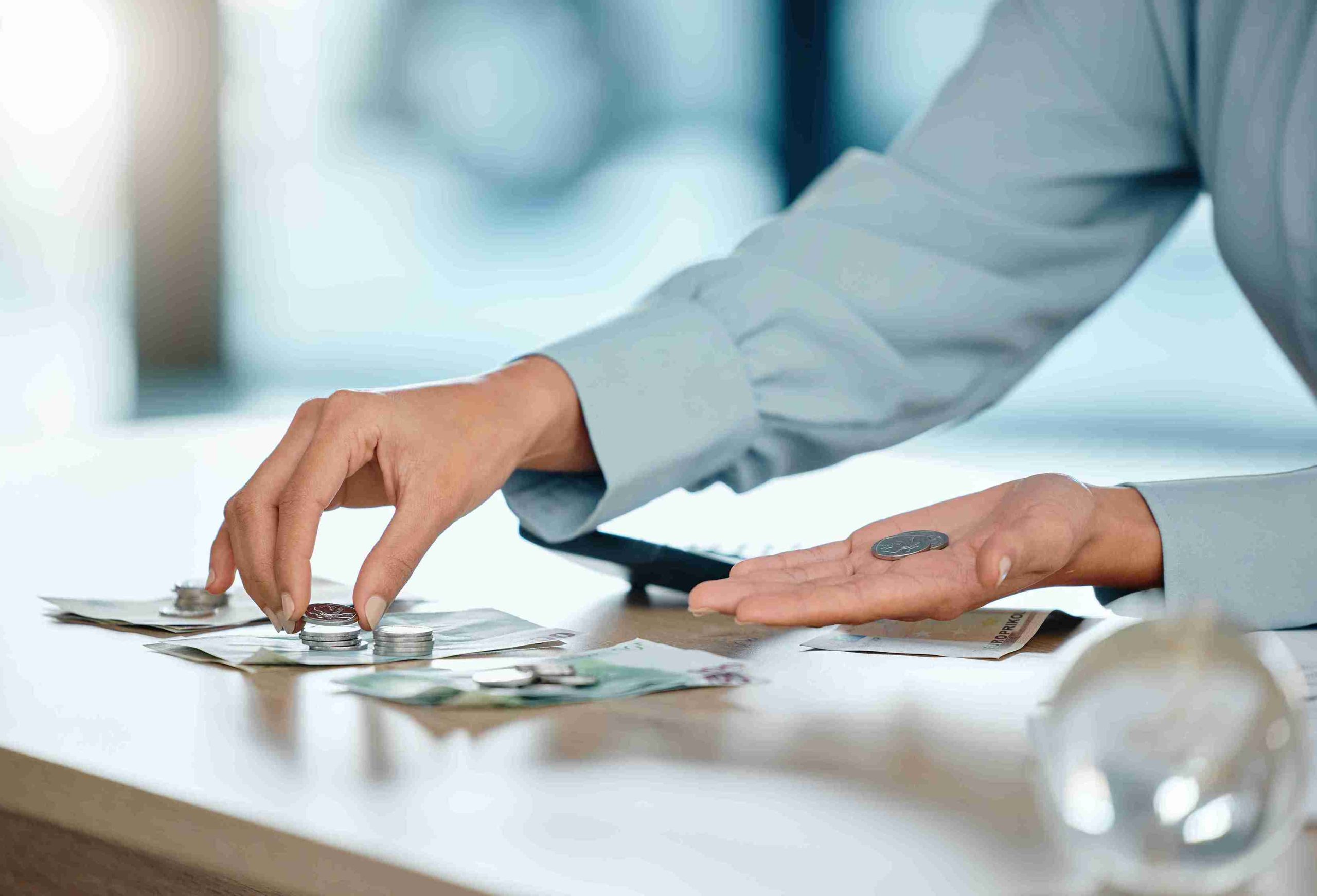 A person counts cash on a table, focusing intently on the bills and coins in front of them.