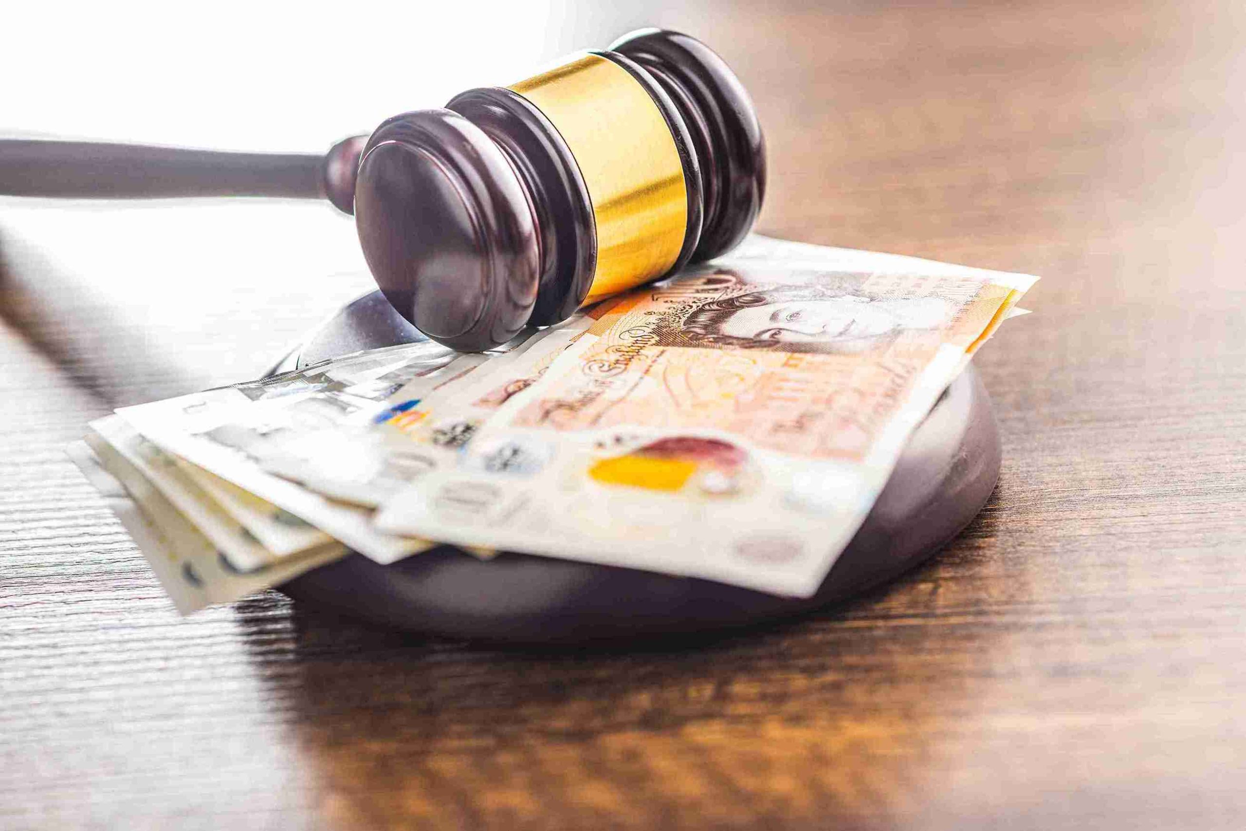 A judge's gavel rests beside stacks of money on a wooden table, symbolizing justice and financial matters.