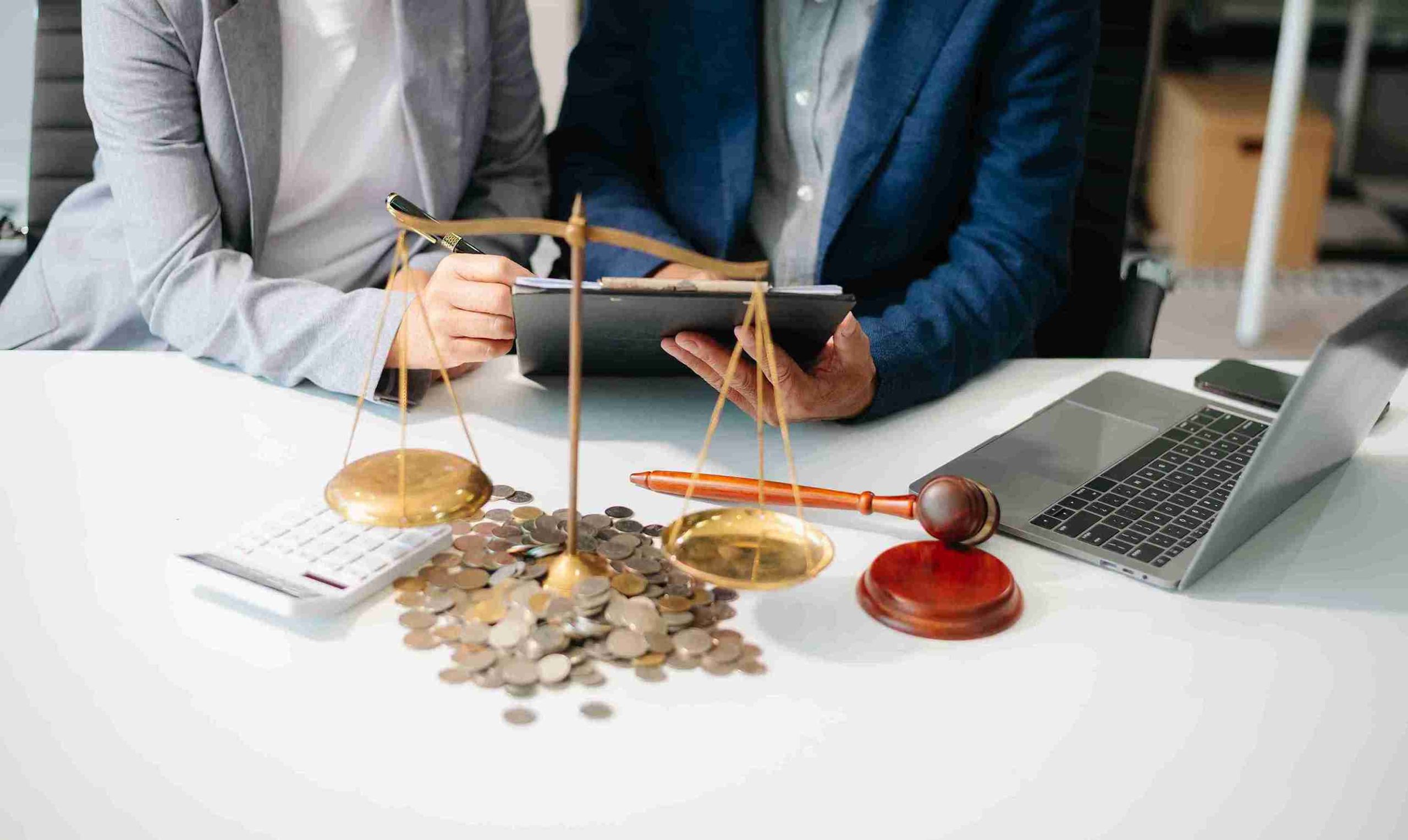 Two business professionals discussing data at a table with a laptop and a scale between them.