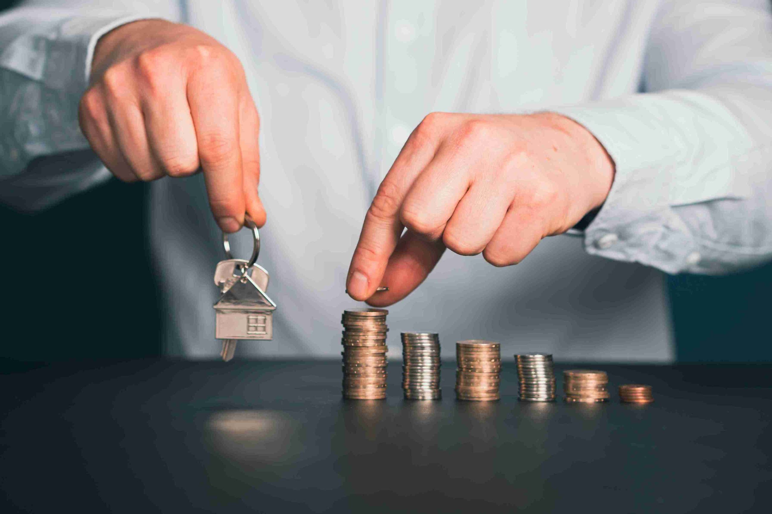 A man holds a house key and coins, symbolizing home ownership and financial investment.