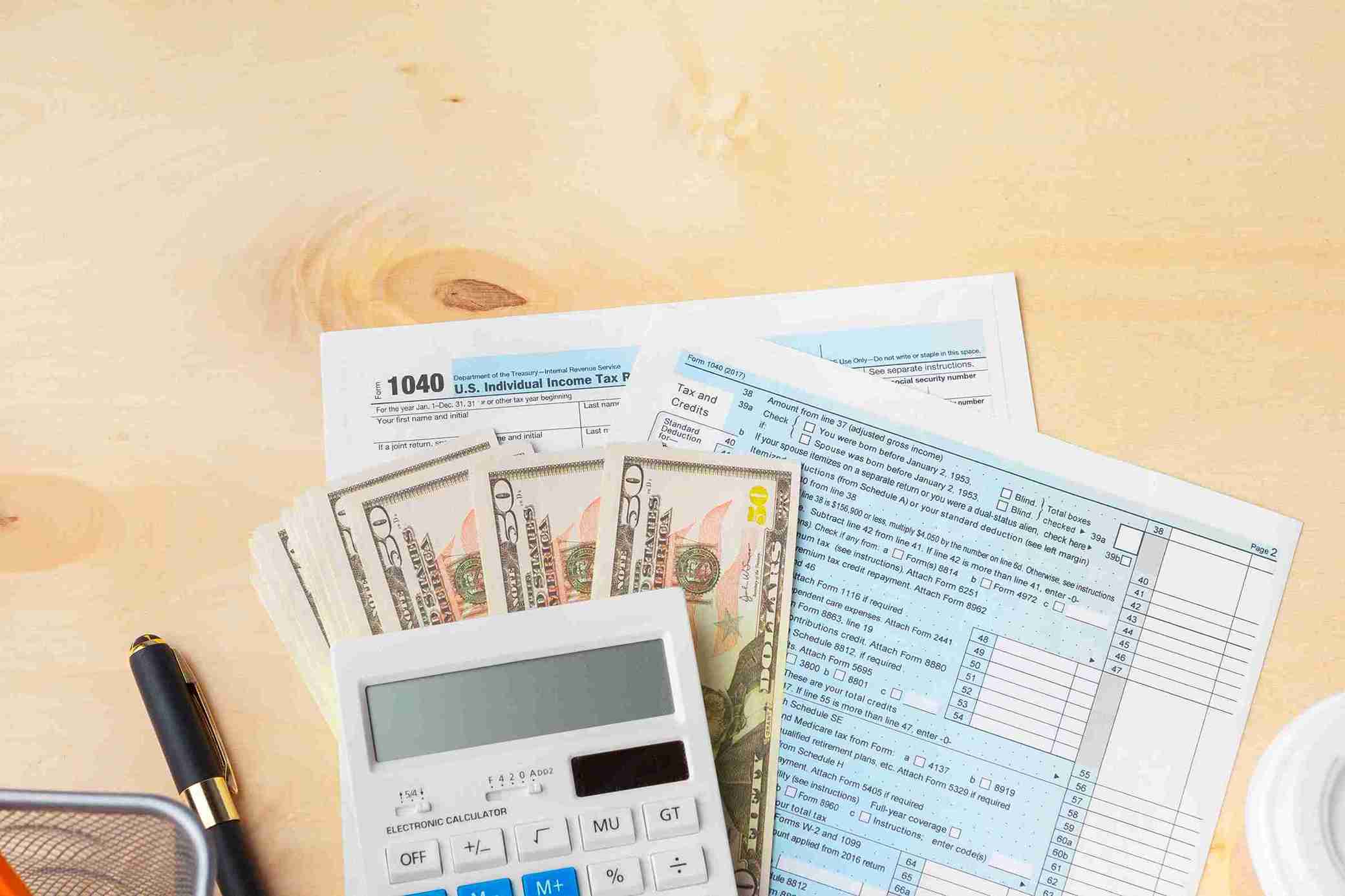 Taxes and financial documents scattered on a wooden desk, with a calculator and a pen nearby.
