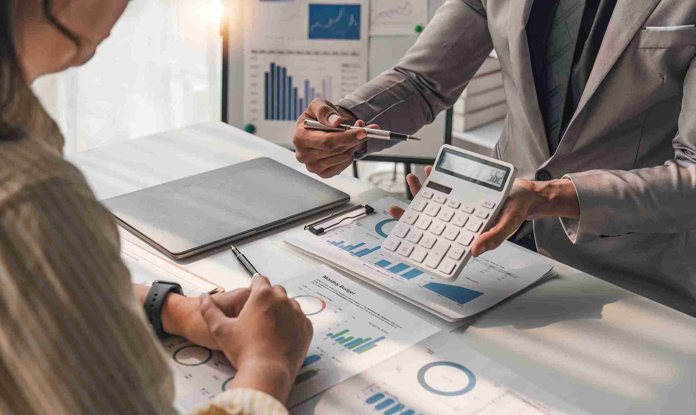 Two people collaborate, using a calculator and a laptop, focused on their work together.