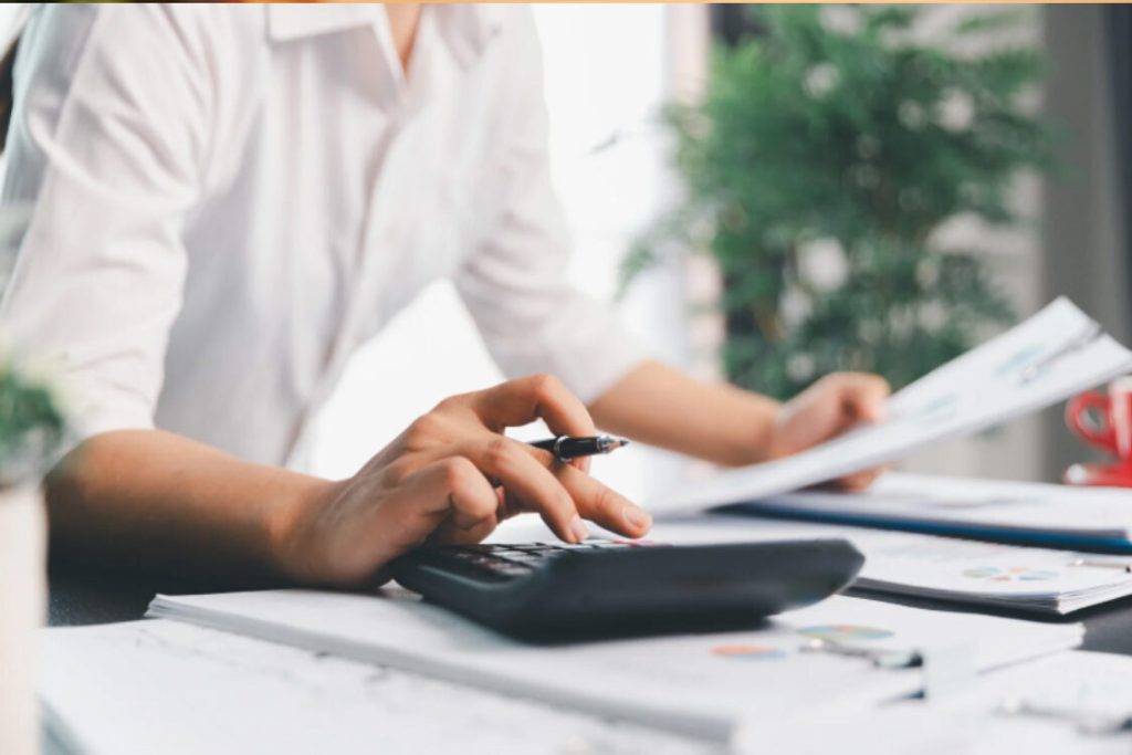 (Close-up of hands pressing a calculator, representing the financial calculations and documentation needed for a tax fraud report.)