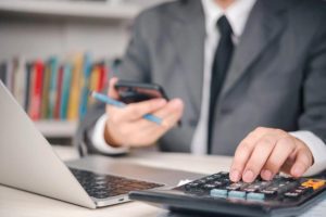 (A business professional calculating how much is corporation tax using a calculator and smartphone in a UK office.)
