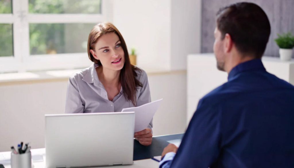 A tax professional in a grey shirt discussing tax residency documents with a male client across a desk, representing a consultation on the double taxation agreement UK.