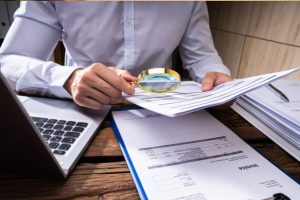 (A person using a magnifying glass to audit an invoice, symbolizing tax fraud investigation.)
