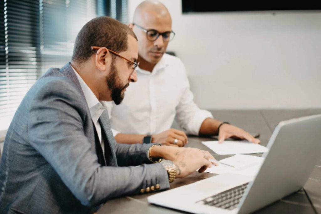 Two business professionals discussing financial paperwork on a laptop, symbolizing tax investigation or legal consultation.