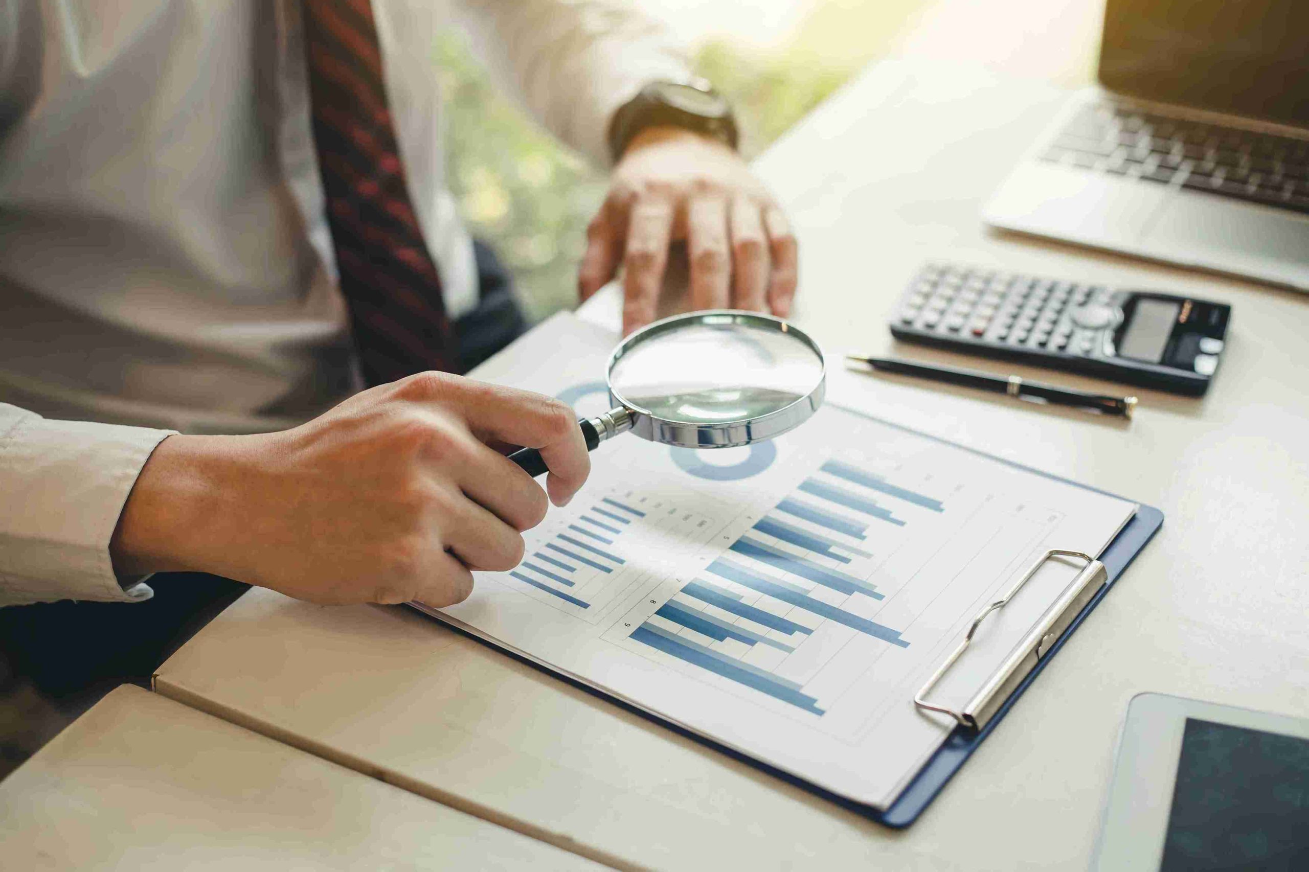 Businessman examining financial data closely with a magnifying glass, highlighting attention to detail in his analysis.