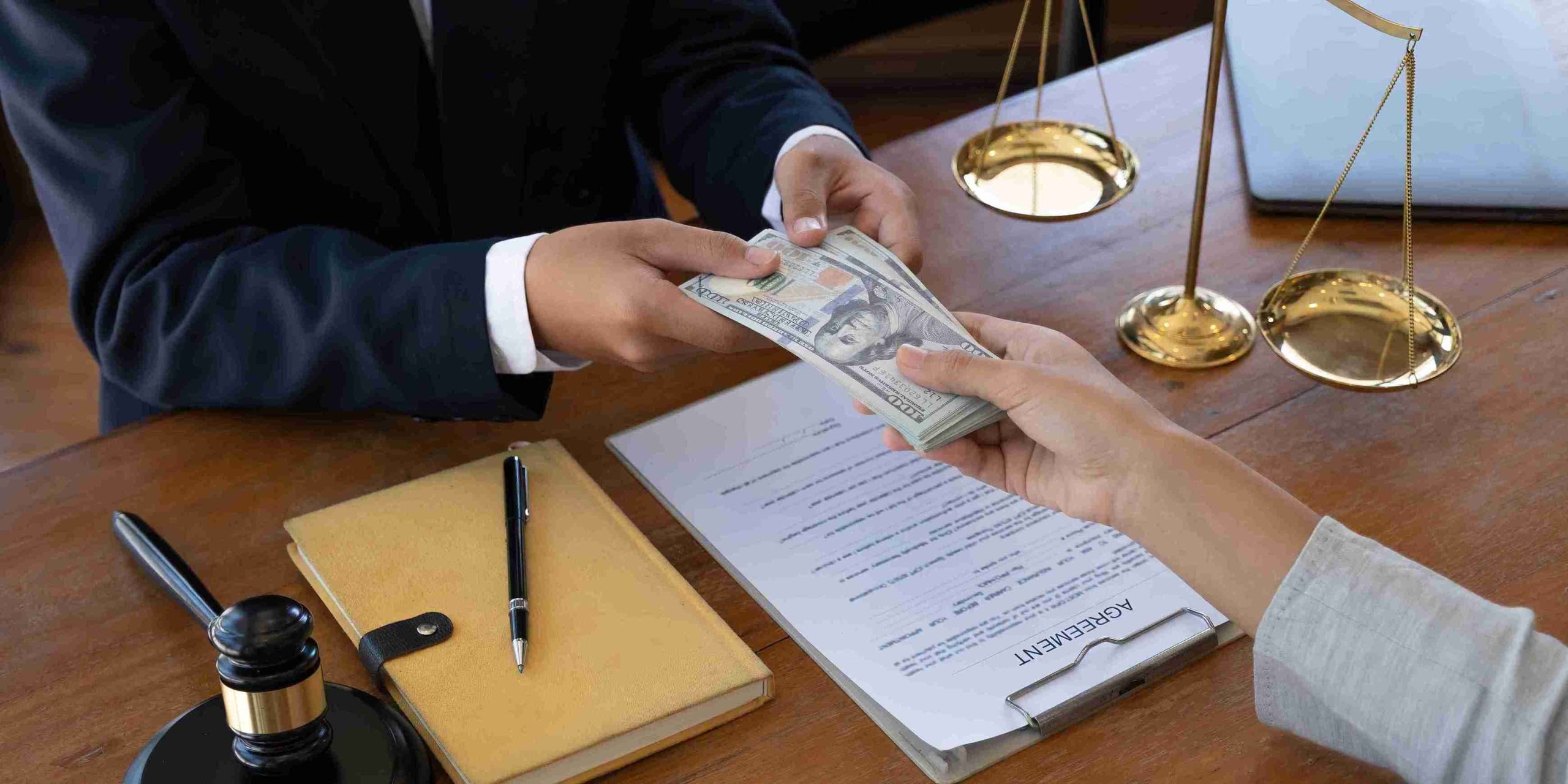 A lawyer hands cash to a client in a professional setting, symbolizing a financial transaction or settlement.