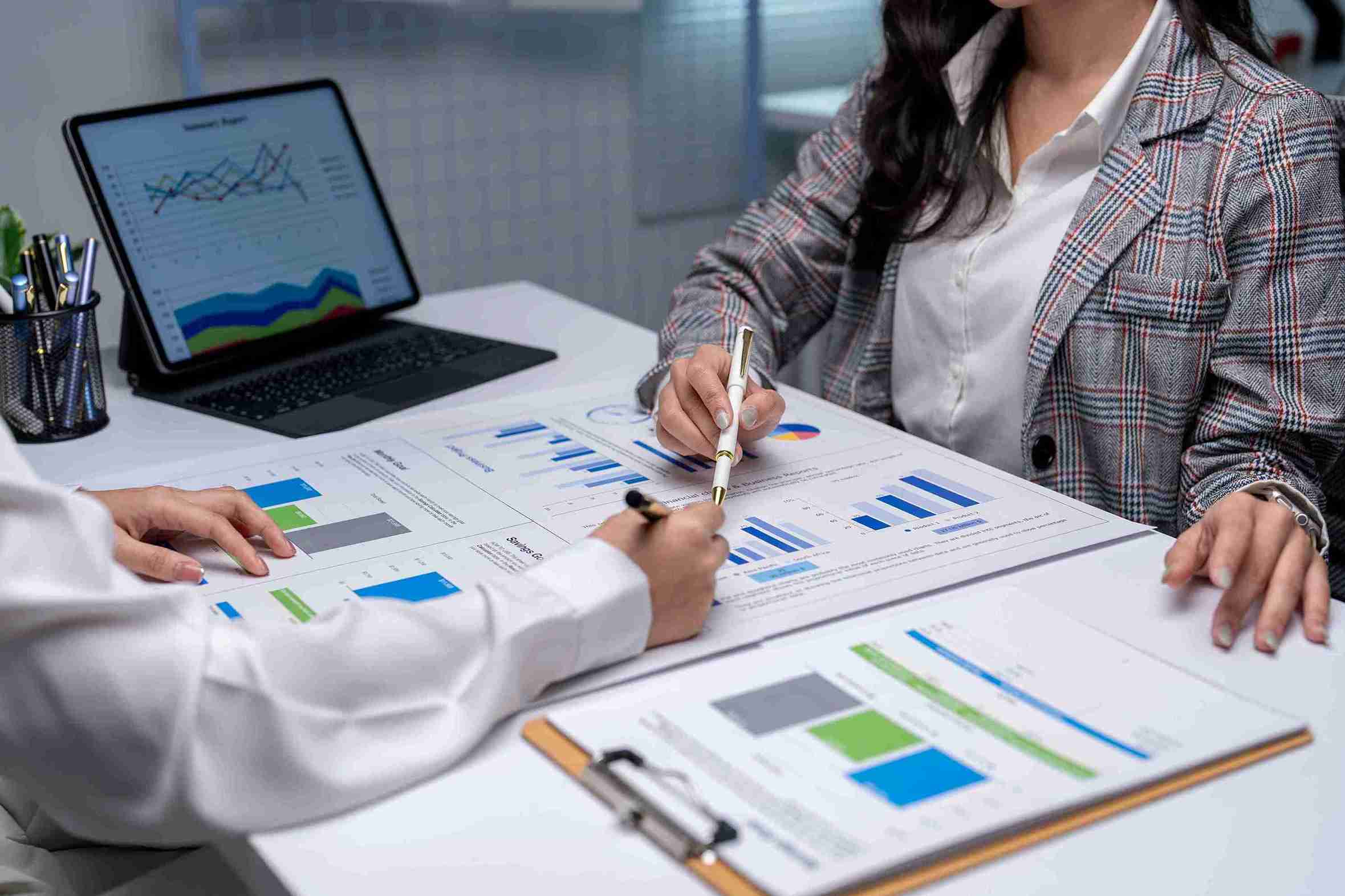 Two businesswomen collaborate at a desk, reviewing documents and discussing ideas in a professional setting.