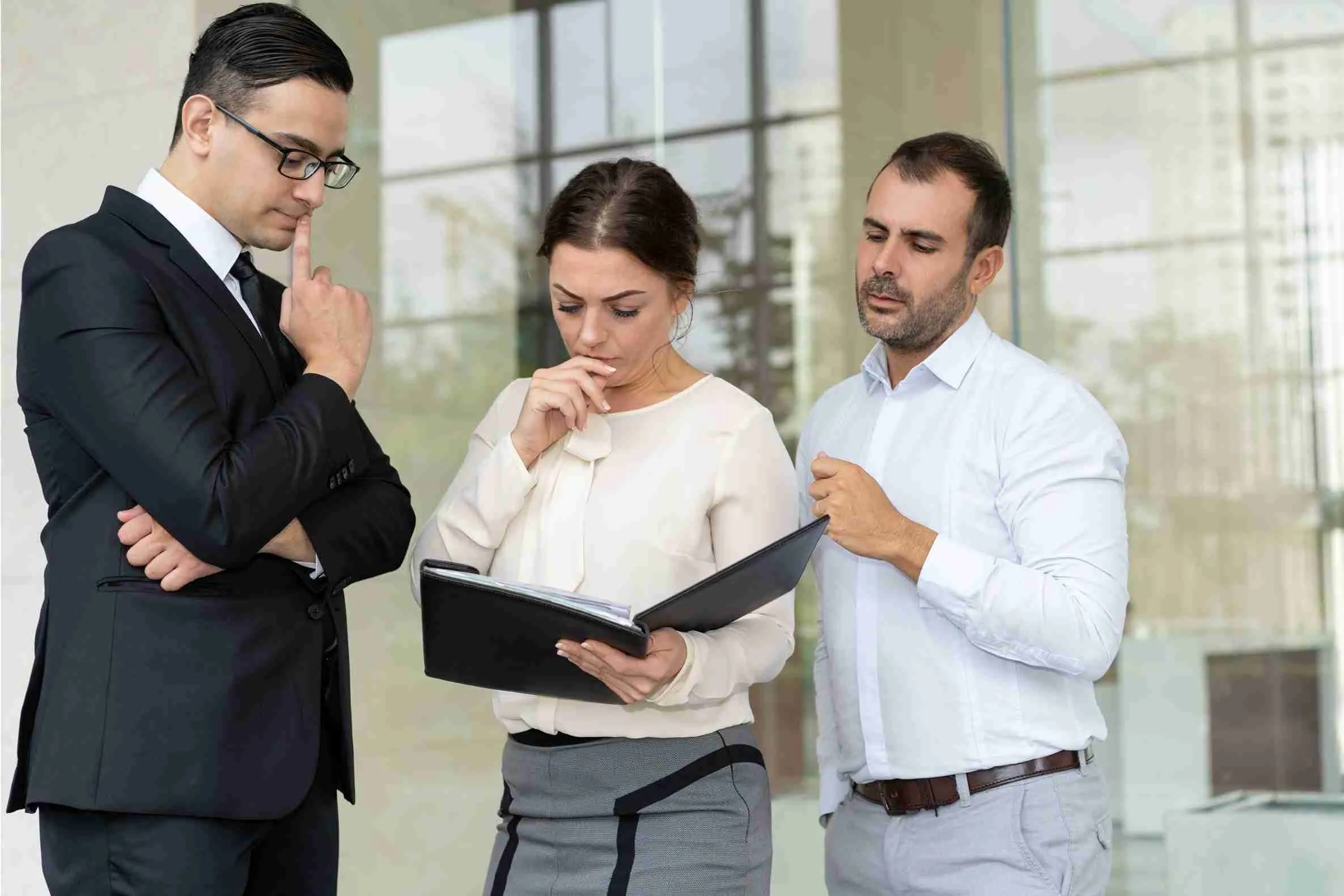 Tax fraud 3 Three business professionals standing together in a modern office, engaged in conversation and collaboration.