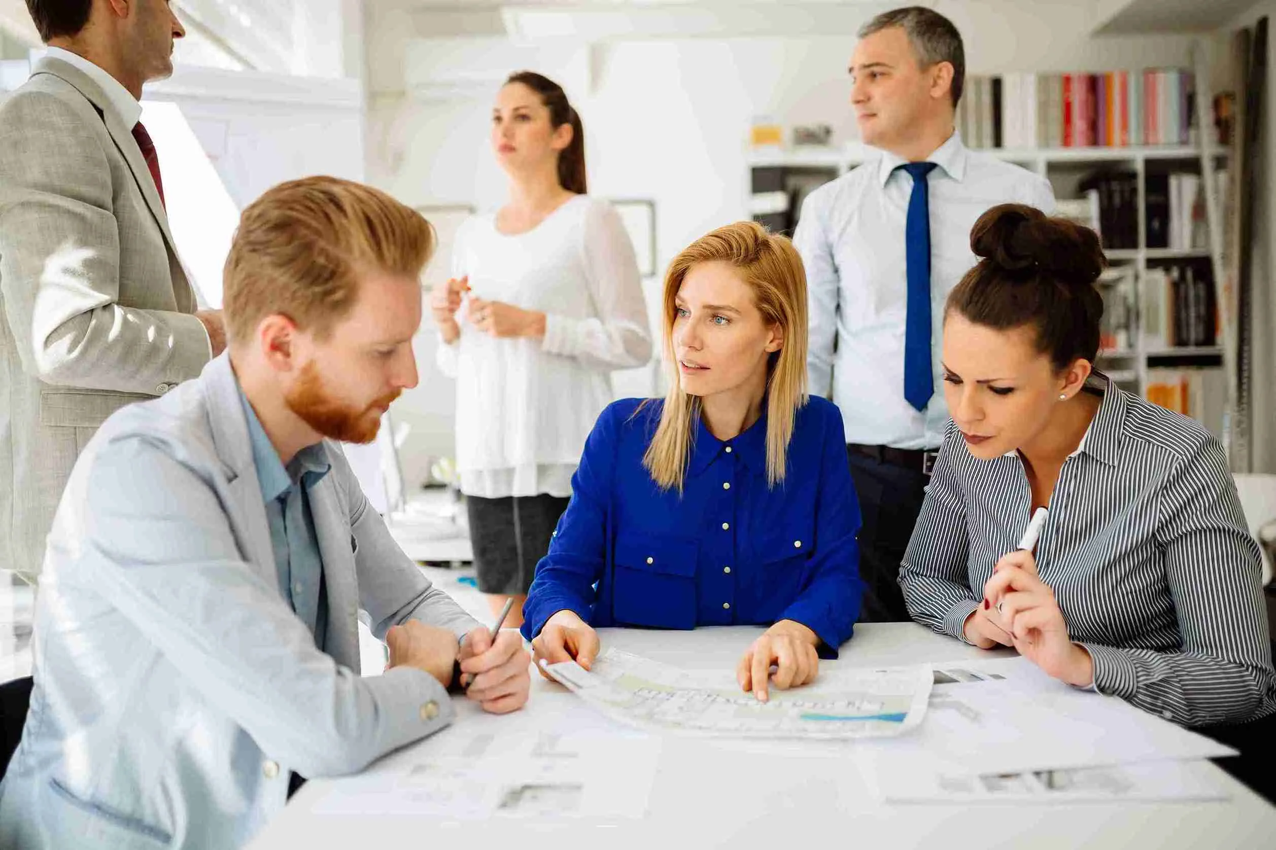 A diverse group of business professionals gathered around a table, reviewing documents and discussing strategies.