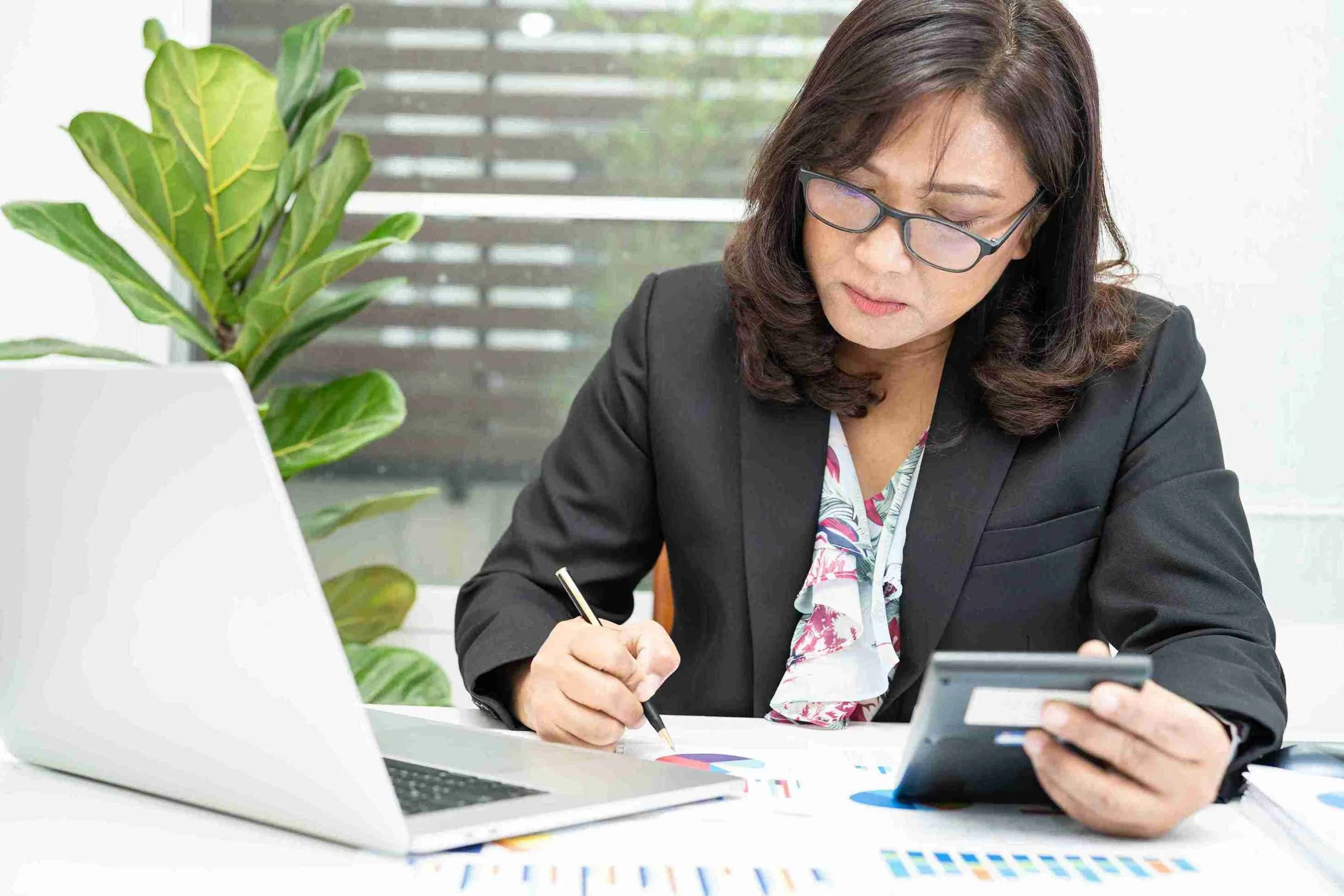 woman in a business suit focused on her laptop, working diligently in a modern office setting.