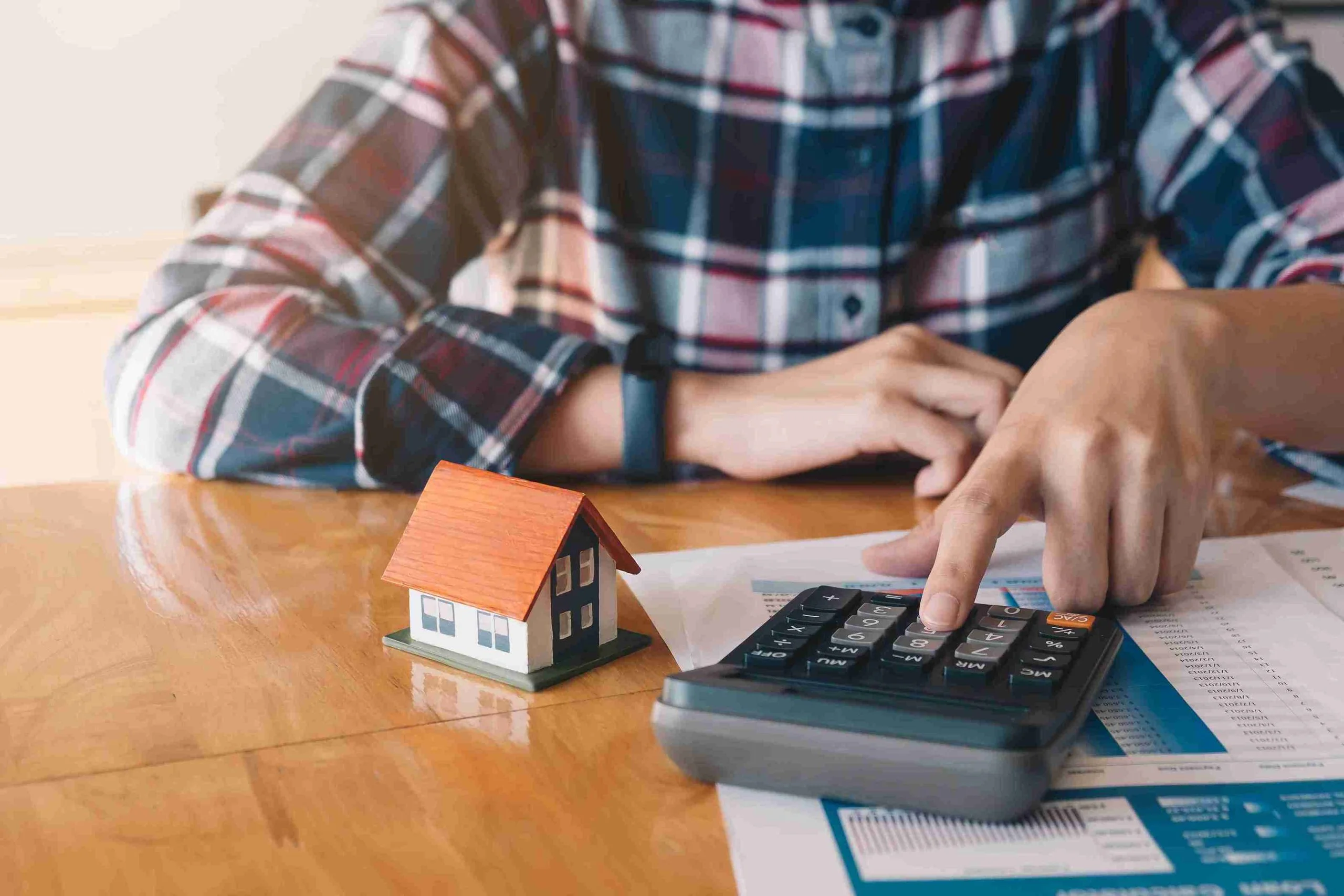A woman focused on a calculator, calculating her mortgage payment with papers and a pen beside her.